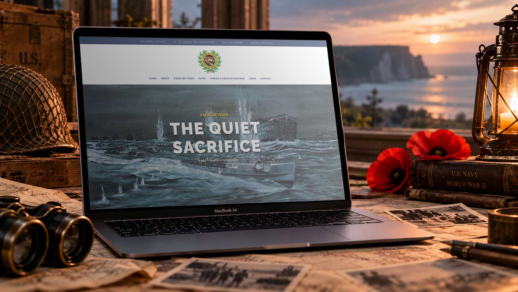 MacBook Air displaying the Exercise Tiger Trust website homepage, surrounded by Second World War memorabilia, historical photographs, maps, red remembrance poppies and a lantern in a commemorative coastal setting at sunset.
